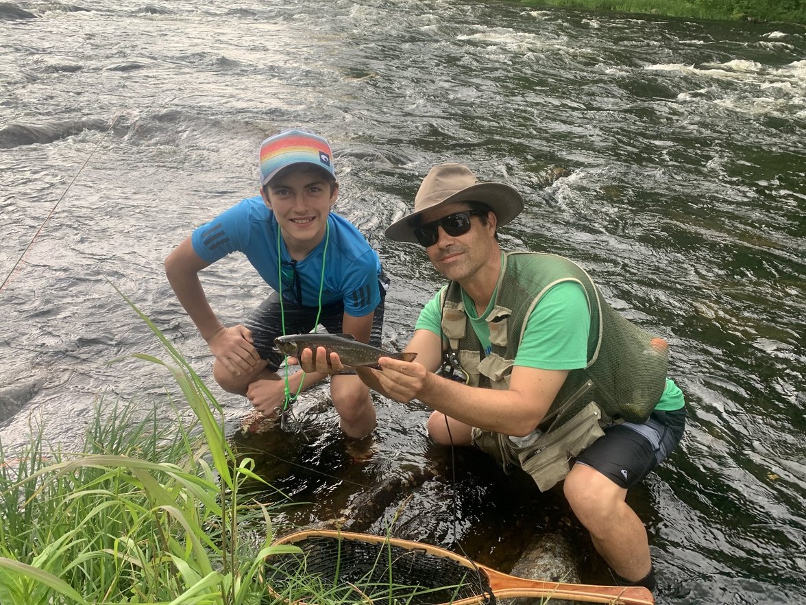 Kevin Bonasera with a Camp Kawanhee camper holding a brook trout beside a river